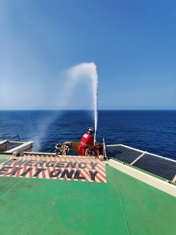 A rescuer conducts a water jet drill on an offshore vessels deck under a clear blue sky.